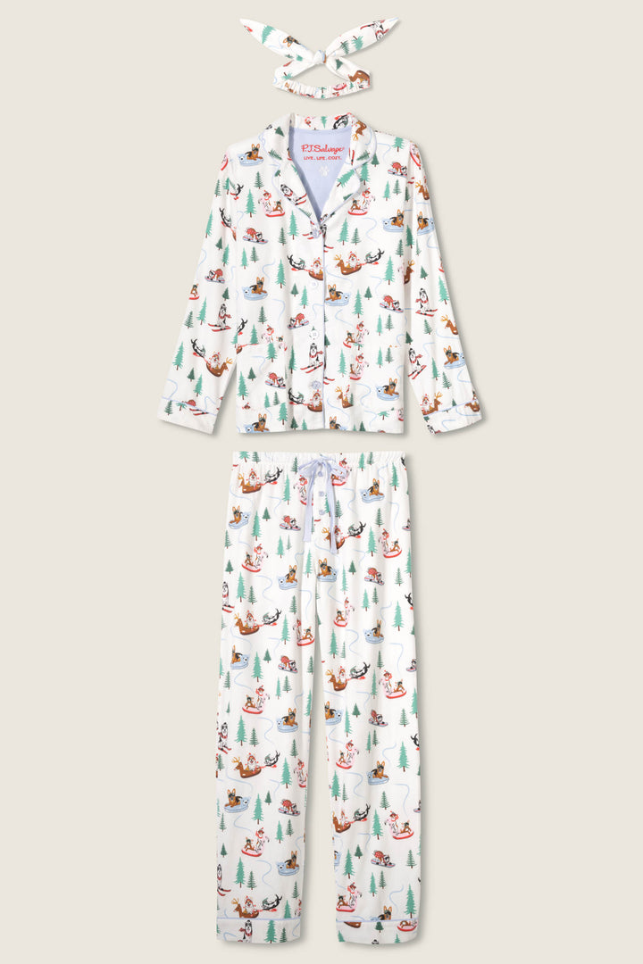 The P.J. Salvage Sleigh All Day Winter Print Flannel PJ Set includes a white button-up top, matching pants, and headband with a colorful holiday dog and tree print, shown on a plain light background.