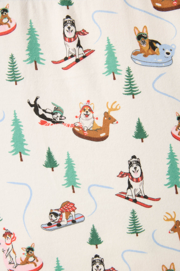 The P.J. Salvage Sleigh All Day Winter Print Flannel Plus Size PJ Set features illustrated dogs enjoying winter sports among green pine trees on a cream background.