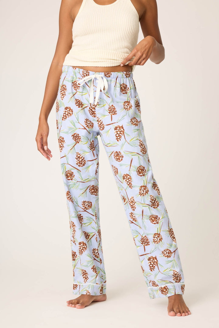 A person stands barefoot against a plain background wearing a cream ribbed tank top and P.J. Salvage Feelin' Pine Pinecone Print Flannel Pant in light blue.