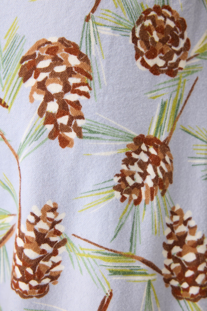A close-up of P.J. Salvage's Feelin' Pine Pinecone Print Flannel Pant, featuring brown pinecones and green pine needles in a repeating pattern on a light blue fabric.