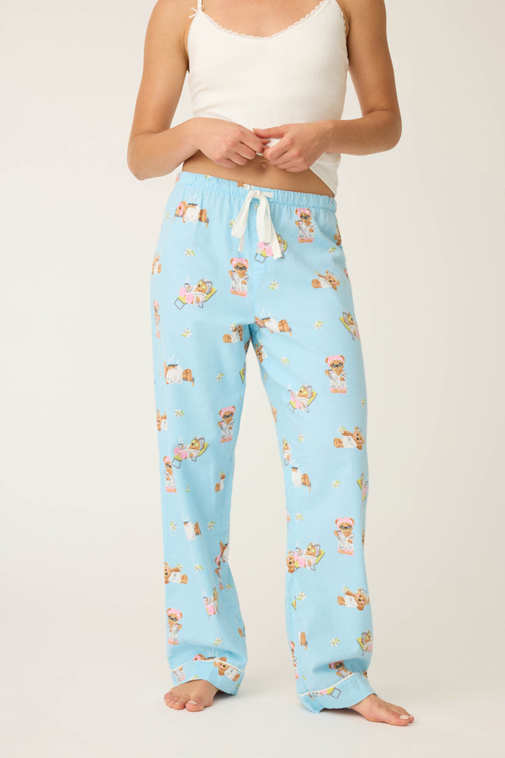 A person stands barefoot against a plain background wearing P.J. Salvage Beary Cute Bear Print Flannel Pants in light blue with a teddy bear print and a white tank top; their face is not visible.