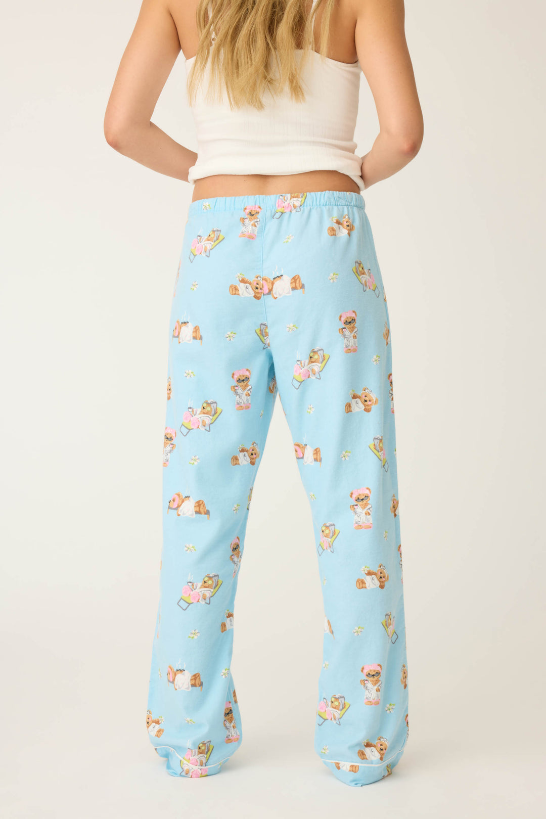 A person with long blonde hair, wearing a white tank top and P.J. Salvage Beary Cute Bear Print Flannel Pants, stands facing away from the camera against a plain background.