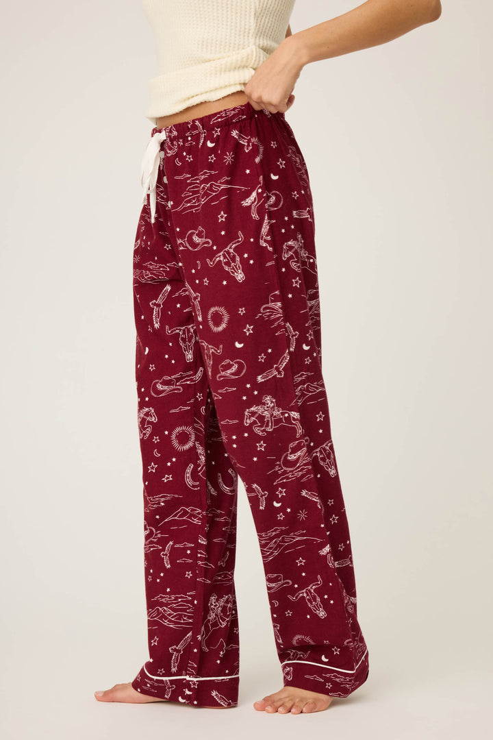A person stands barefoot wearing P.J. Salvages DOGS PANT FLANNELS in port, featuring a maroon hue with an allover print. Only the torso and legs are visible against a plain background, paired with a cream ribbed tank top.