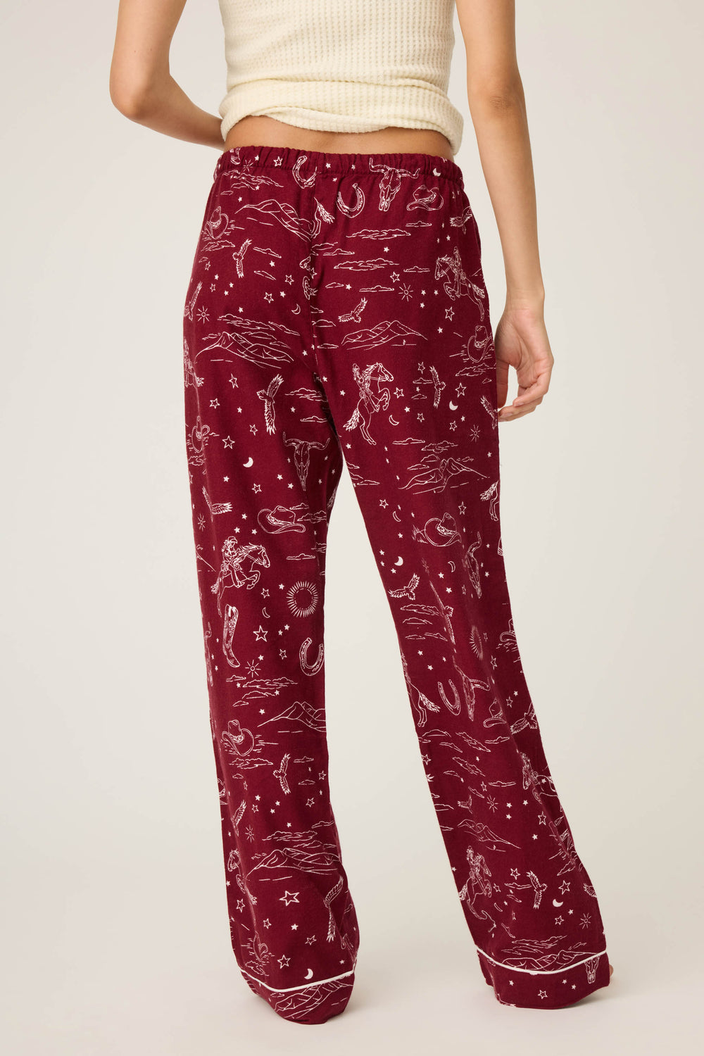 A person stands with their back to the camera, wearing P.J. Salvage DOGS PANT FLANNELS in port—a maroon pajama pant—paired with a cream ribbed sleeveless top. The background is plain and light-colored.