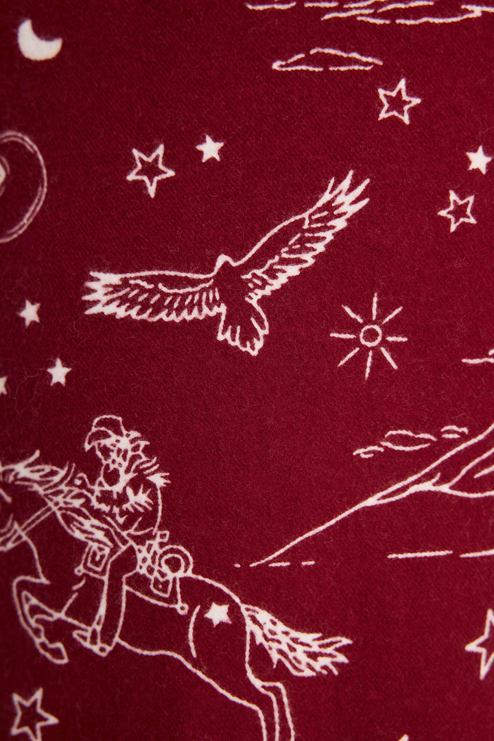White line drawing on dark red DOGS PANT FLANNELS - port by P.J. Salvage, featuring a cowboy on horseback, an eagle, stars, clouds, and a sun in a Western-themed pattern.