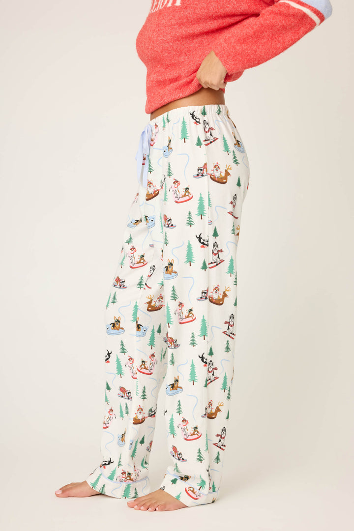 A person stands barefoot wearing P.J. Salvage Sleigh All Day Winter Print Flannel Pants and a red long-sleeve top. Their head is out of frame.