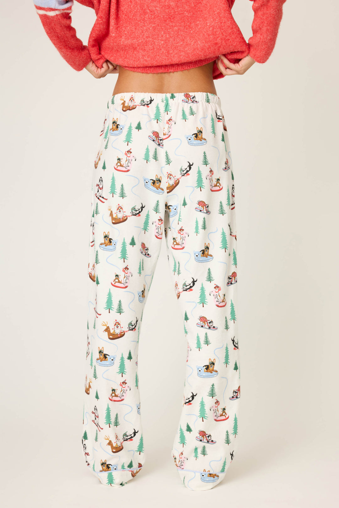 A person models the P.J. Salvage Sleigh All Day Winter Print Flannel Pant, featuring a playful sledding dog and tree pattern, shown waist down against a plain background.