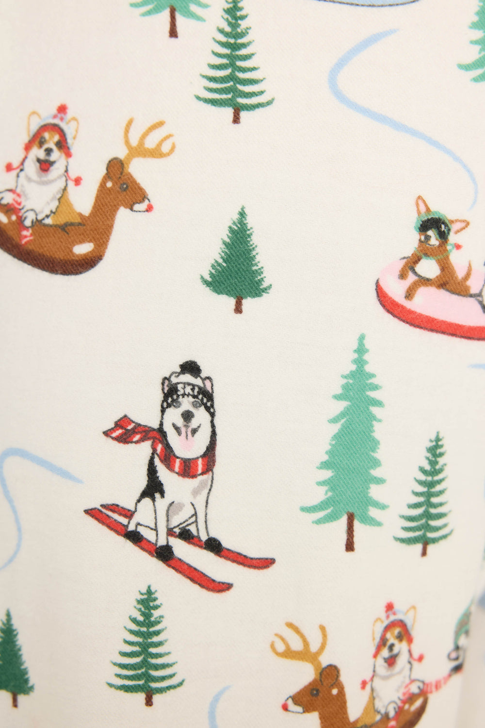 The P.J. Salvage Sleigh All Day Winter Print Flannel Pant features cartoon dogs skiing, tubing, and riding a reindeer amid pine trees and blue wavy lines on a white background.