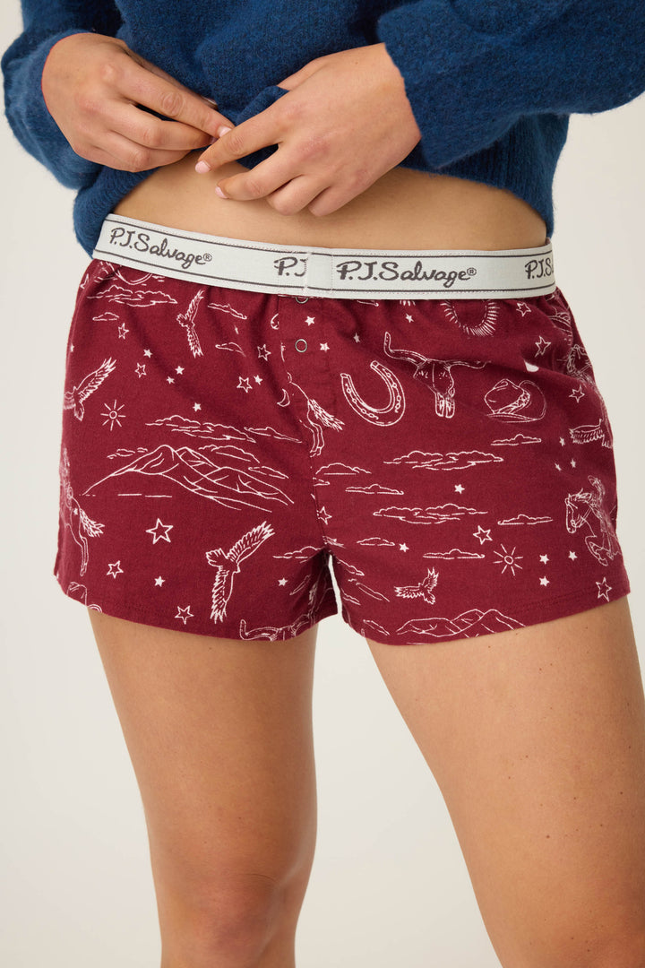 A person wearing maroon P.J. Salvage SHORT FLANNELS with white western-themed line drawings and a blue sweater. The photo is cropped to show only the lower torso and upper legs.