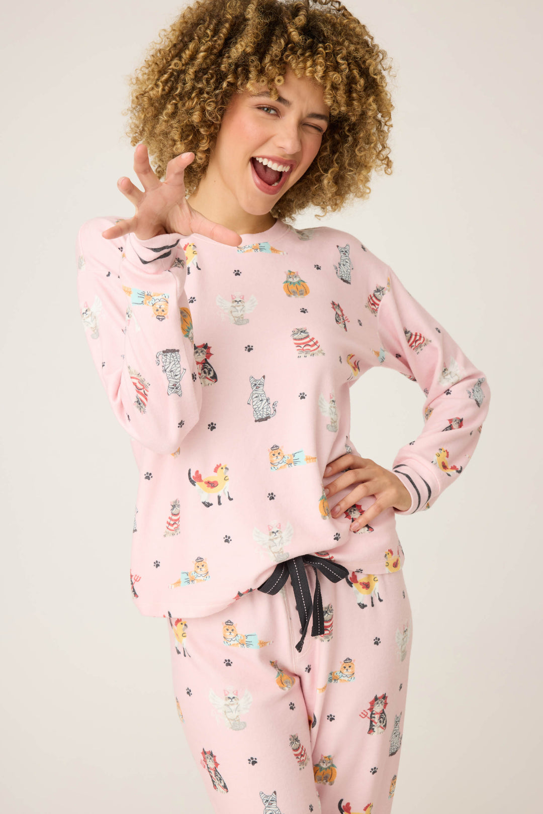 A person with curly hair in the P.J. Salvage CATS PJ SET FELINE SPOOKY poses playfully against a plain background, winking, smiling, and holding one hand up.