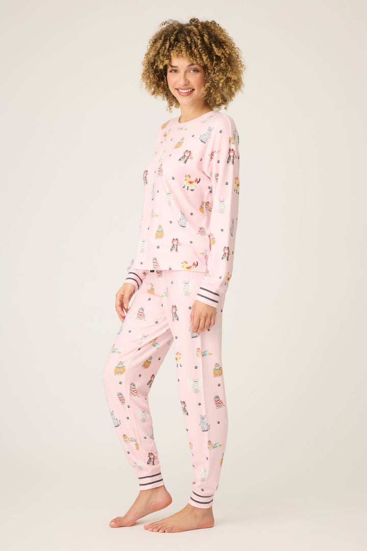 A person with curly hair stands barefoot against a plain background, smiling at the camera while wearing the P.J. Salvage CATS PJ SET FELINE SPOOKY.