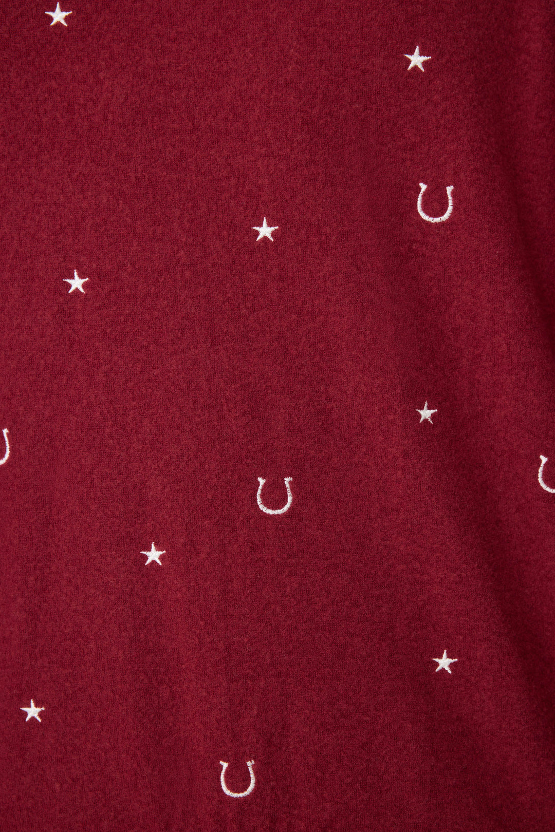 A close-up of P.J. Salvages Pant Set HORSE SHOE PJ SET HOLD YOUR HORSES shows red fabric with small white stars and horseshoe symbols evenly spaced across the surface.