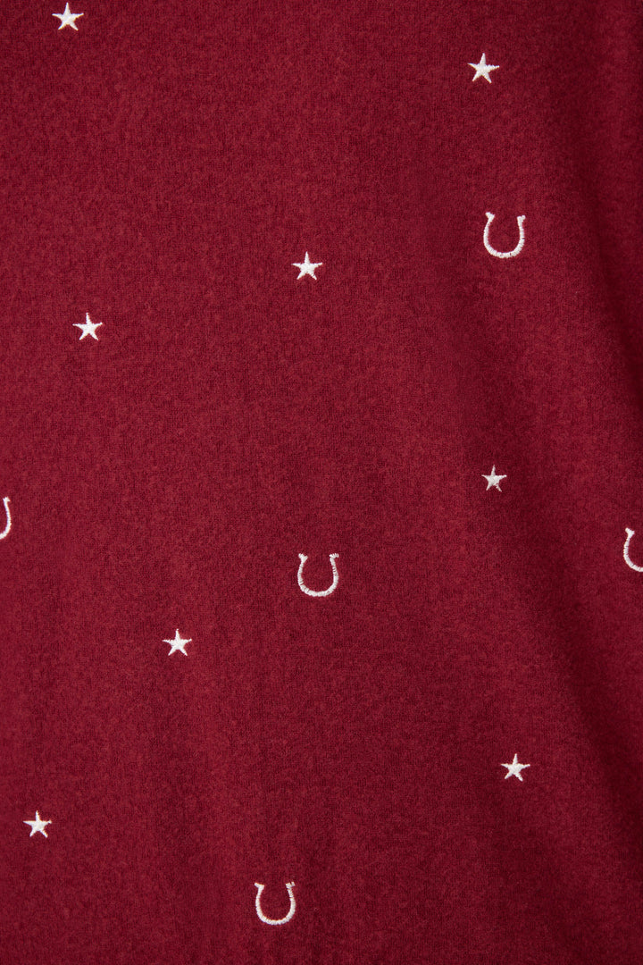 A close-up of P.J. Salvages Pant Set HORSE SHOE PJ SET HOLD YOUR HORSES shows red fabric with small white stars and horseshoe symbols evenly spaced across the surface.