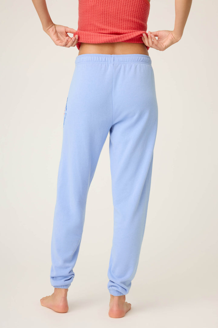A person stands barefoot, facing away from the camera, wearing P.J. Salvages SOLID BANDED PANT LADY LUCK in light blue and a red textured top, which they lift slightly to show their lower back.