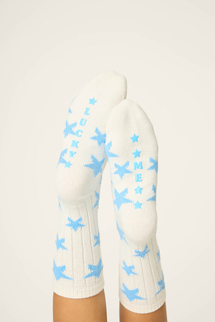A pair of feet in P.J. Salvage STAR SOCKS LADY LUCK, featuring white socks with blue stars and “FUCK ME” printed in blue on the soles, shown against a plain background.