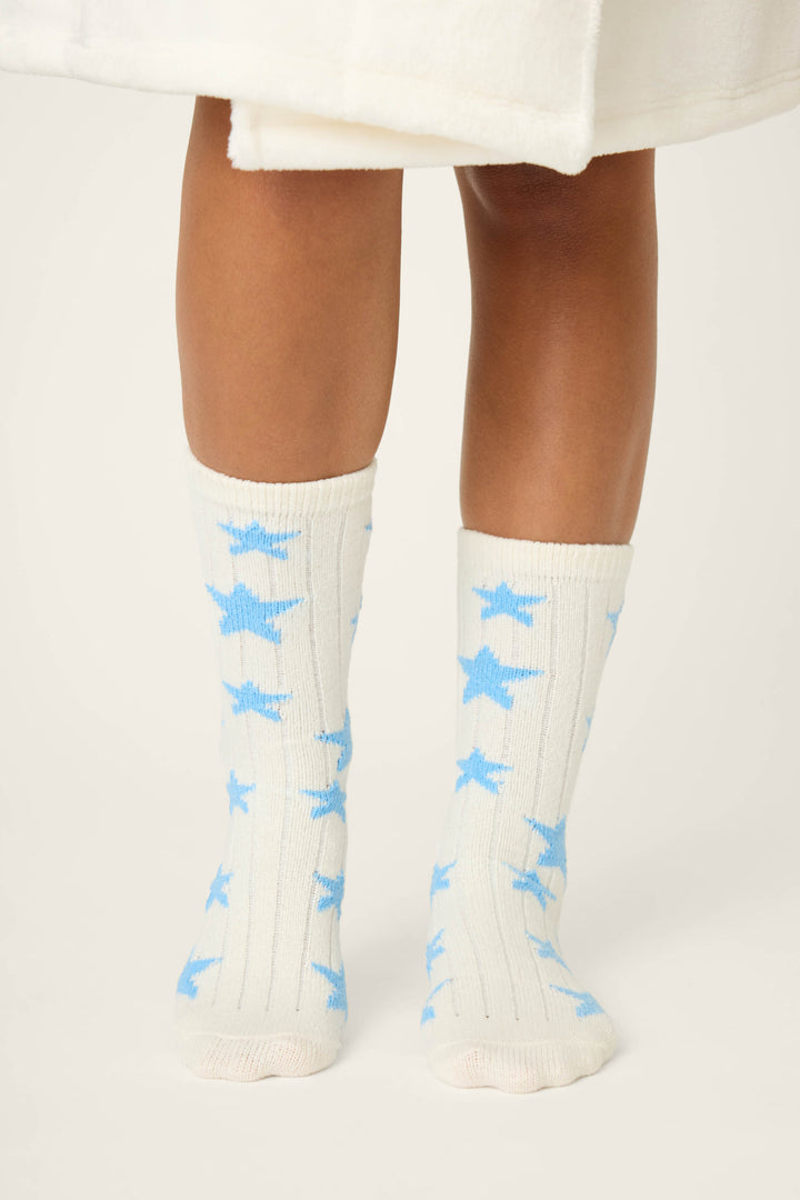 A person stands on a light background wearing P.J. Salvage STAR SOCKS LADY LUCK—cream-colored socks with blue star patterns. Only the lower legs and feet are visible, partially covered by a white garment at the knees.