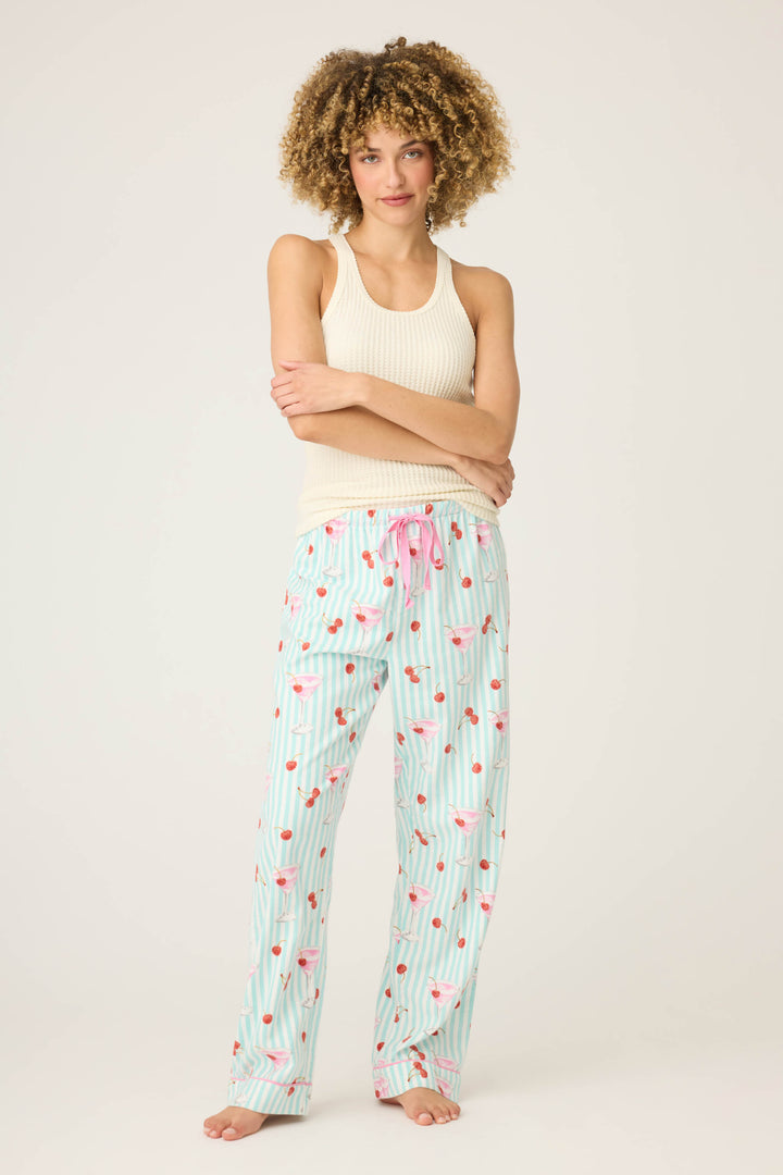 A person with curly hair stands barefoot against a plain background, wearing a cream ribbed tank top and P.J. Salvage DOGS PANT FLANNELS, arms crossed over their chest.