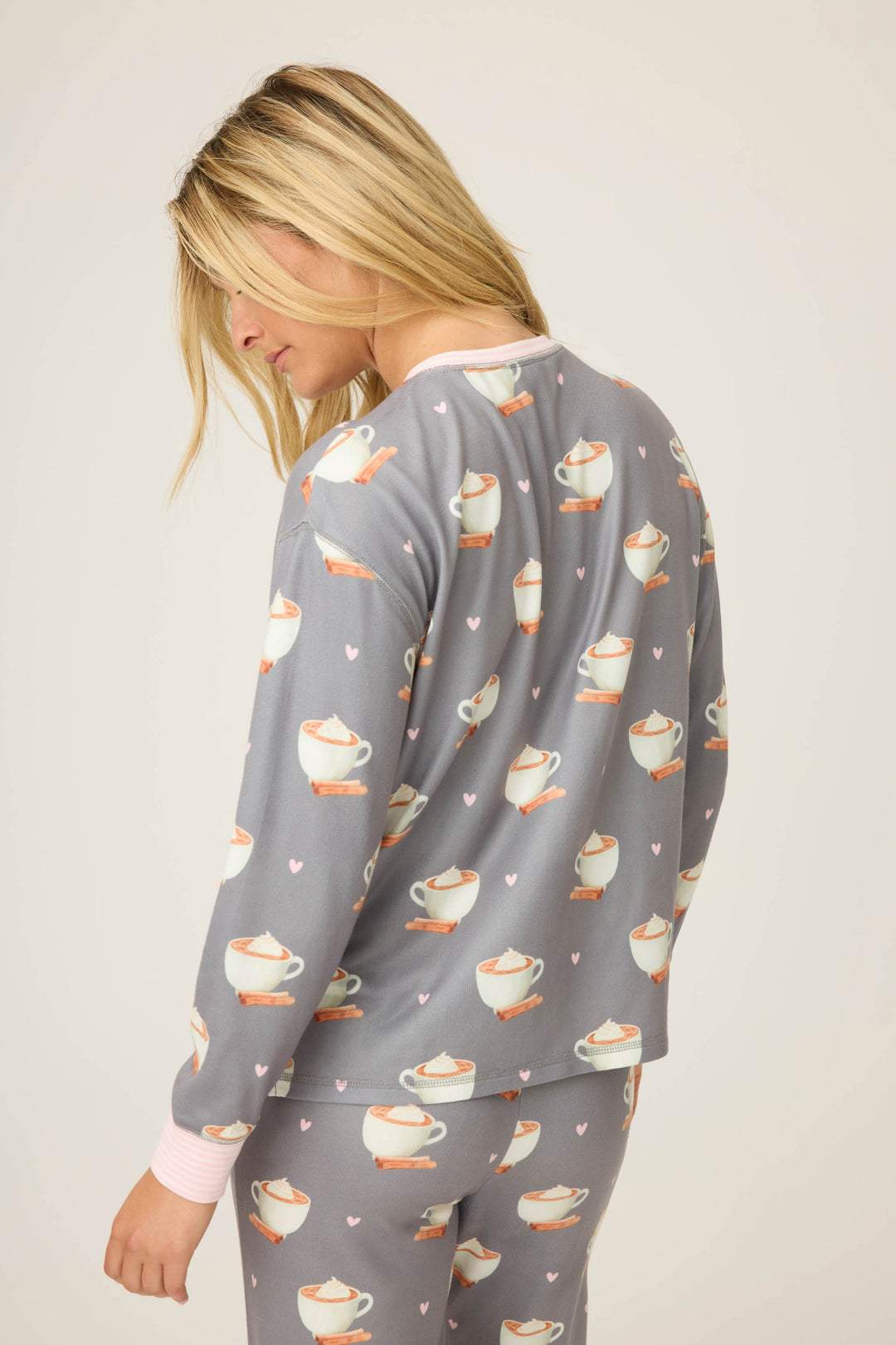 A woman with long blonde hair wears the P.J. Salvage Love You A Latte Coffee Print Long Sleeve Top, featuring cups and pink hearts, while facing slightly away from the camera against a plain background.