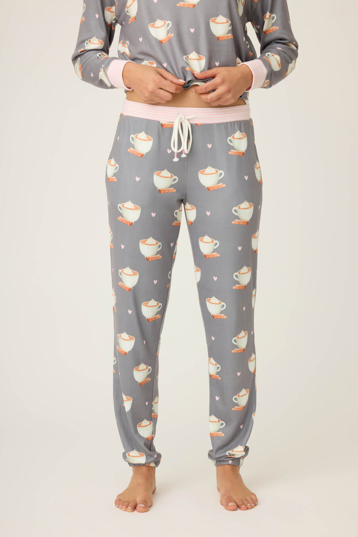 Model wears the P.J. Salvage Love You A Latte Coffee Print Banded Pant—gray pajama pants with teacup and heart print, pink waistband with white drawstring—and matching top, barefoot against a plain light background.