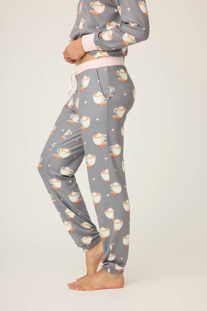 A person stands barefoot in P.J. Salvage Love You A Latte Coffee Print Banded Pants—gray pajama pants with a white mug and heart pattern. The matching pajama top is partially visible against a plain, light background.