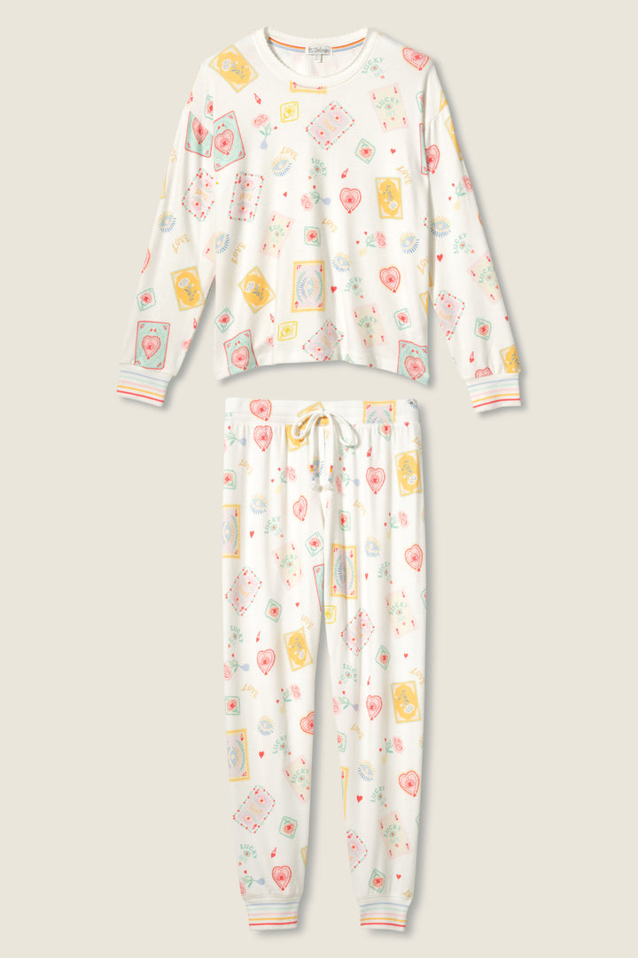 The P.J. Salvage LUCKY PJ SET LUCKY ME features a white matching pant set with playful prints of playing cards, envelopes, and hearts. The long-sleeved top and drawstring pants include ribbed cuffs accented with pastel stripes.