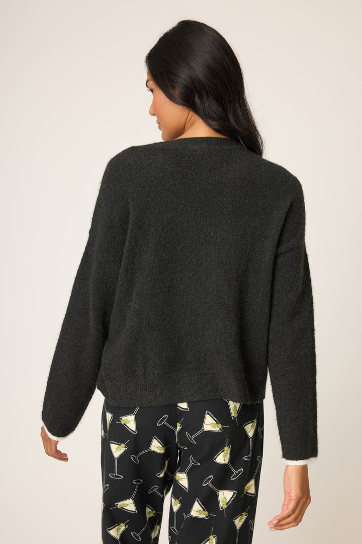 A woman with long dark hair is seen from the back, wearing the P.J. Salvage Merrier With A Martini Snuggle Sweater and matching martini glass print pants, standing against a plain light background.