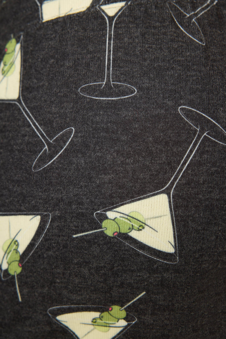 A close-up of the P.J. Salvage Merrier With A Martini Short, featuring dark fabric printed with martini glasses filled with yellow liquid and green olives on toothpicks.
