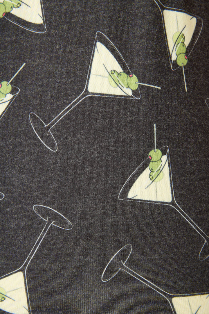 A close-up of the Merrier With A Martini Tank Top by P.J. Salvage, showcasing a repeating pattern of martini glasses with green olives on toothpicks against a dark background.