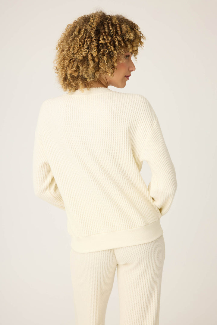 A person with curly hair faces away from the camera, wearing the P.J. Salvage Morning Waffles Solid Ivory Long Sleeve Top against a plain light background.
