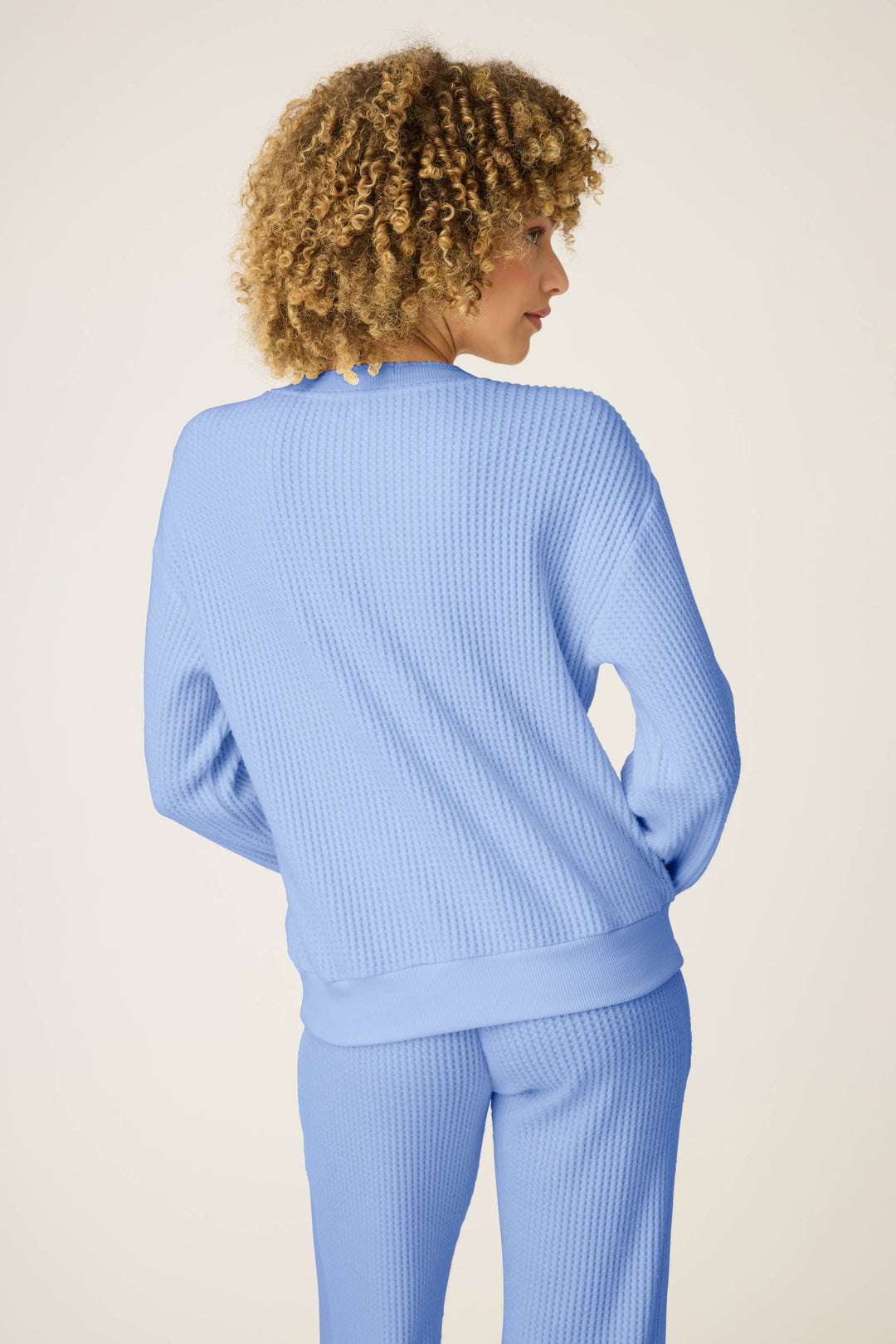 A person with curly hair is seen from the back, wearing the P.J. Salvage Morning Waffles Solid Peri Long Sleeve Top, standing against a plain off-white background.