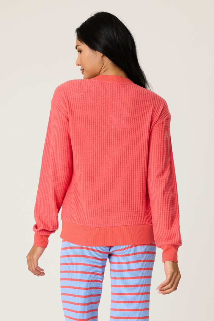 A person with long, dark hair is shown from the back, wearing the P.J. Salvage Morning Waffles Scarlet Long Sleeve Top and blue pants with red horizontal stripes against a plain light background.