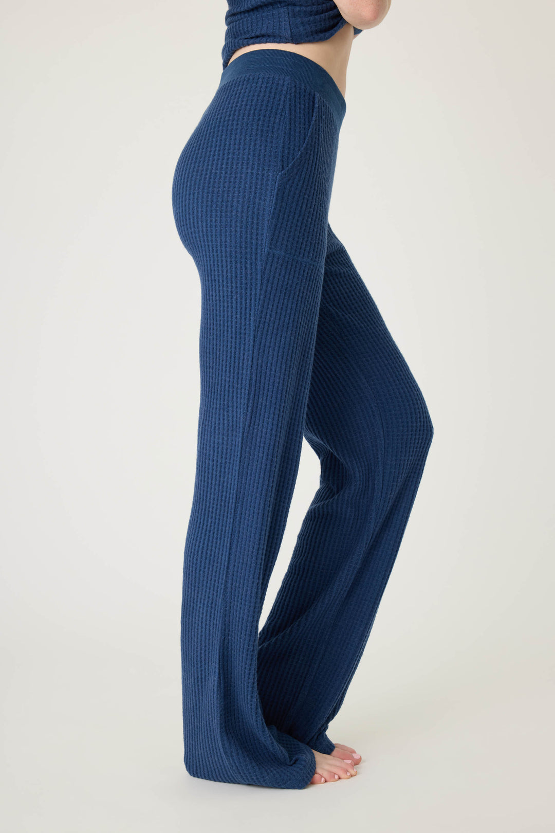Person wearing P.J. Salvage’s Morning Waffles Solid Navy Open Leg Pant with high waist, wide-leg fit, textured fabric, and pockets; standing barefoot on a white background with only lower torso and legs visible.