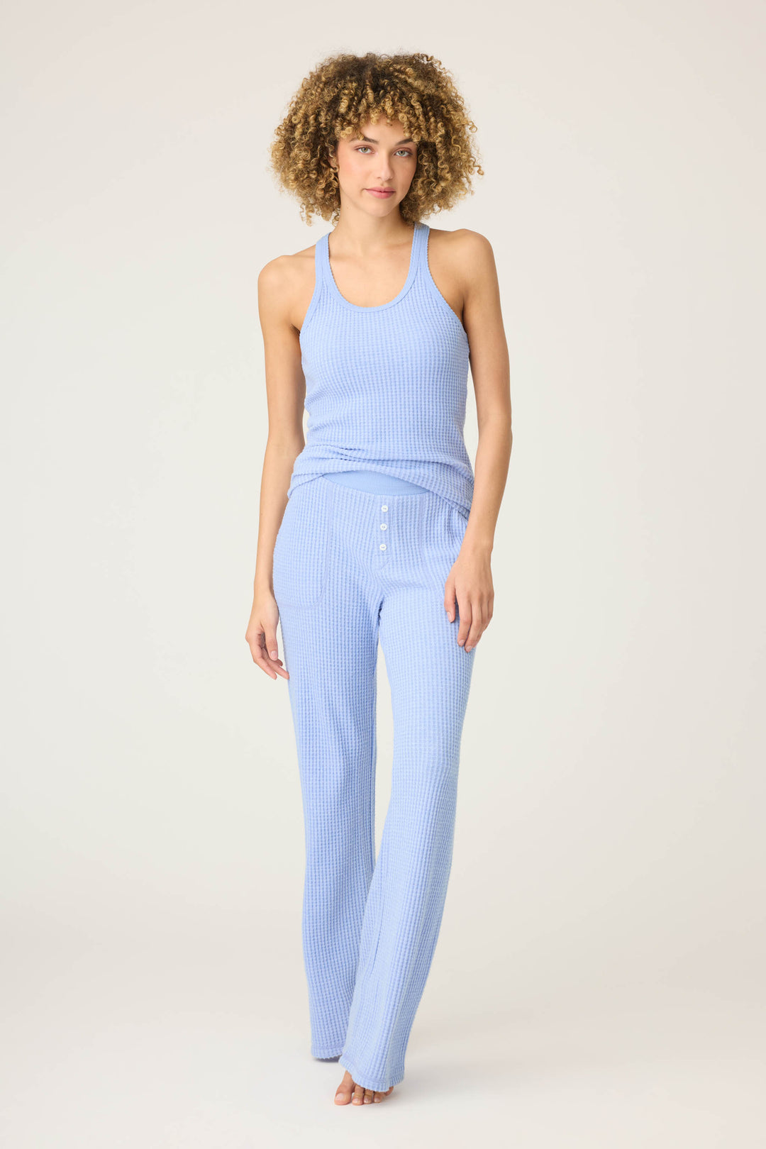 A person stands barefoot against a plain background, wearing the P.J. Salvage Morning Waffles Solid Peri Open Leg Pant with button detail at the waist and a matching ribbed tank top.