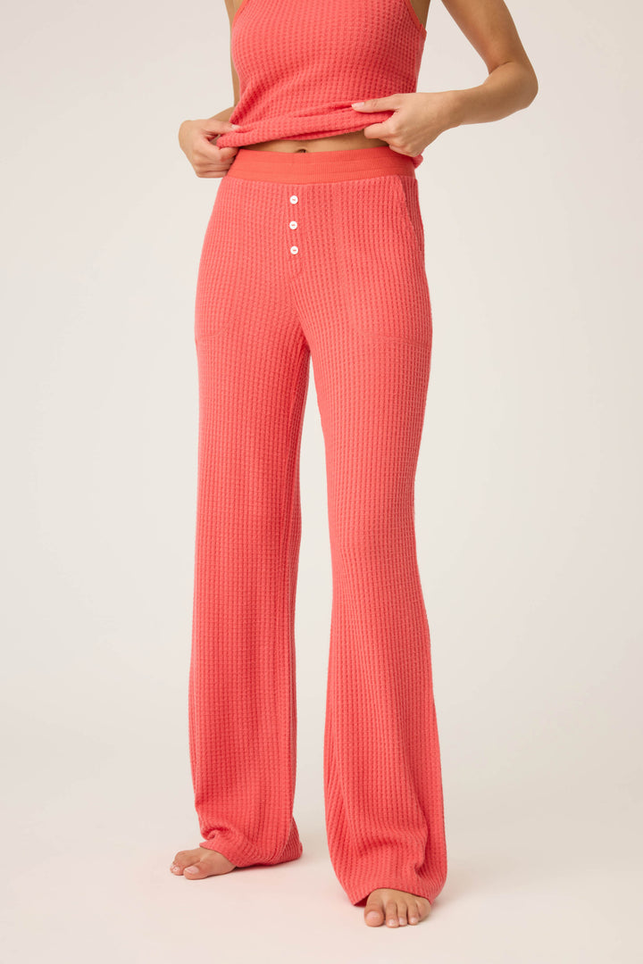 A person wears the P.J. Salvage Morning Waffles Scarlet Open Leg Pant—high-waisted, textured pink lounge pants with three white front buttons—and a matching top. They are barefoot, with their face not visible.