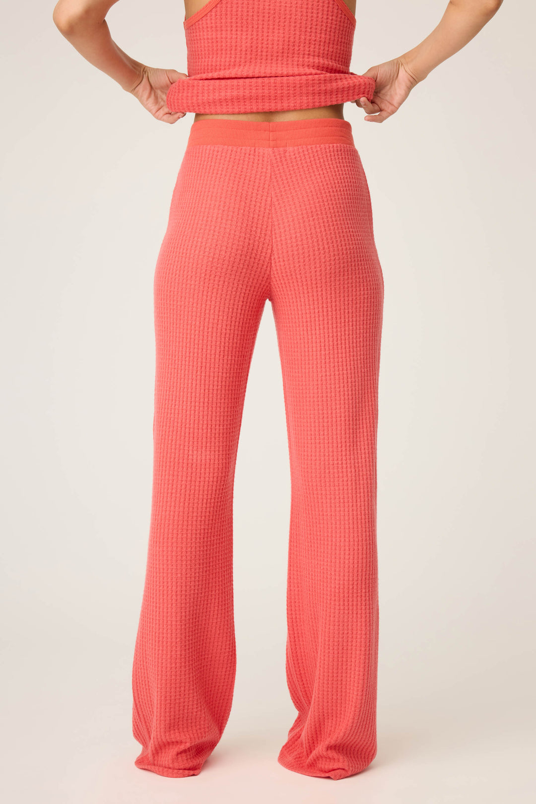 A person in P.J. Salvage's Morning Waffles Scarlet Open Leg Pant stands facing away, slightly lifting their matching top to reveal the textured high-waisted waistband.
