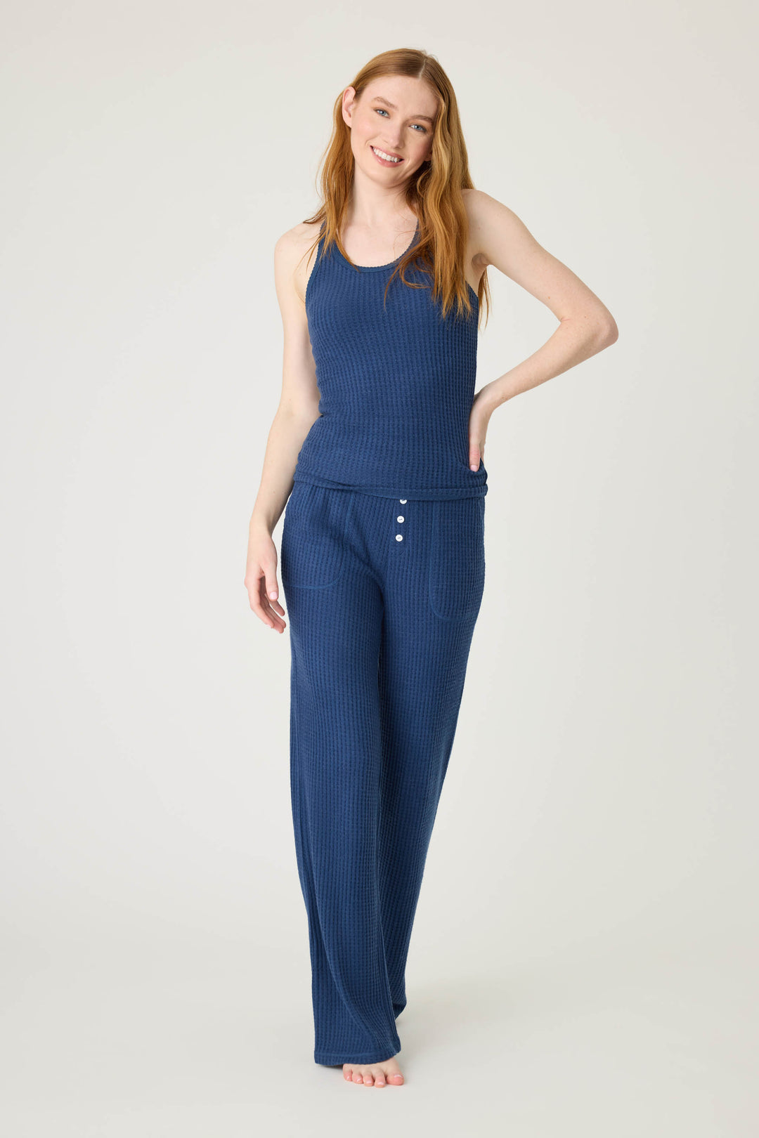 A woman with long red hair stands barefoot against a plain light background, wearing the P.J. Salvage Morning Waffles Solid Navy Tank Top and matching wide-leg pants with button detail at the waist.