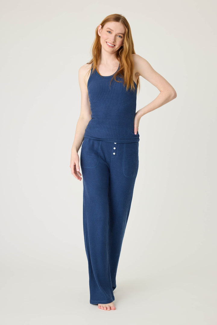 A woman with long red hair stands barefoot against a plain light background, wearing the P.J. Salvage Morning Waffles Solid Navy Tank Top and matching wide-leg pants with button detail at the waist.
