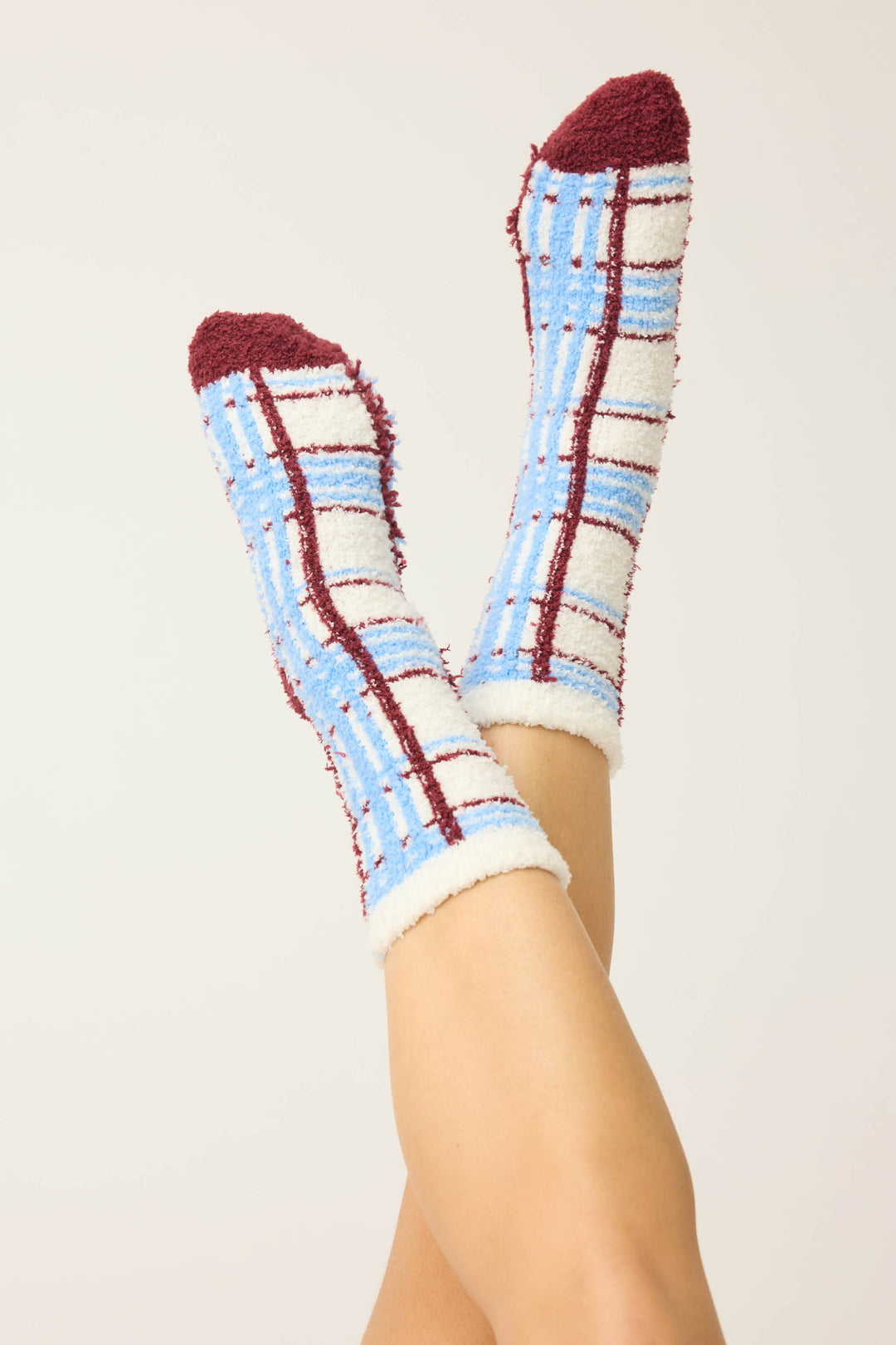 Crossed legs in P.J. Salvage PLAID SOCKS RUFF ON THE RANGE, featuring fuzzy blue, white, and burgundy plaid with burgundy toes, heels, and cuffs against a plain light background.