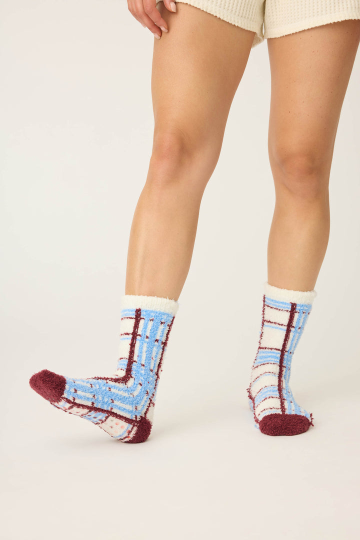A person models the P.J. Salvage PLAID SOCKS RUFF ON THE RANGE—burgundy and white plaid fuzzy socks—paired with cream shorts, set against a plain light background. Only their lower body and legs are shown.