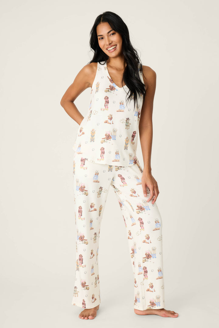 A woman stands barefoot against a plain background, smiling and wearing the P.J. Salvage DOGS V-Neck Tank Ruff On The Range cream pajama set with a sleeveless top and long pants featuring small animal prints.