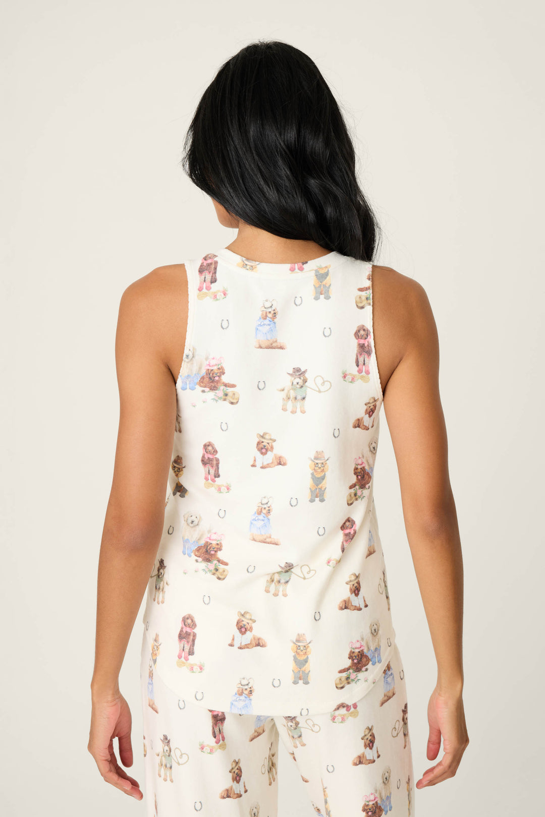 A person with long, dark hair is seen from the back wearing P.J. Salvages DOGS V-Neck Tank Ruff on the Range—a cream-colored, sleeveless top with a dog and horseshoe print. The matching pajama pants are partially visible.