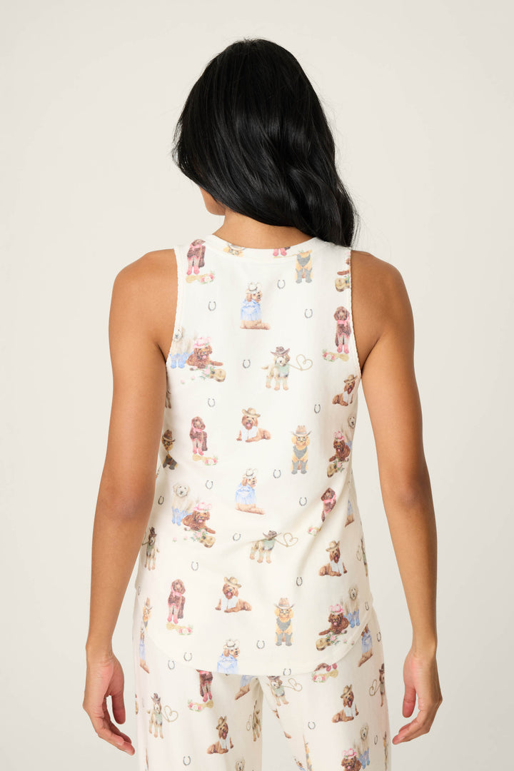 A person with long, dark hair is seen from the back wearing P.J. Salvages DOGS V-Neck Tank Ruff on the Range—a cream-colored, sleeveless top with a dog and horseshoe print. The matching pajama pants are partially visible.