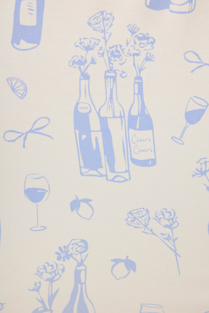 The Parisian Dreams Whimsical Print Open Leg Pant by P.J. Salvage features blue line drawings of wine bottles, flowers, glasses, lemons, and bows on a light background—one bottle’s label reads Cheers Cheers.