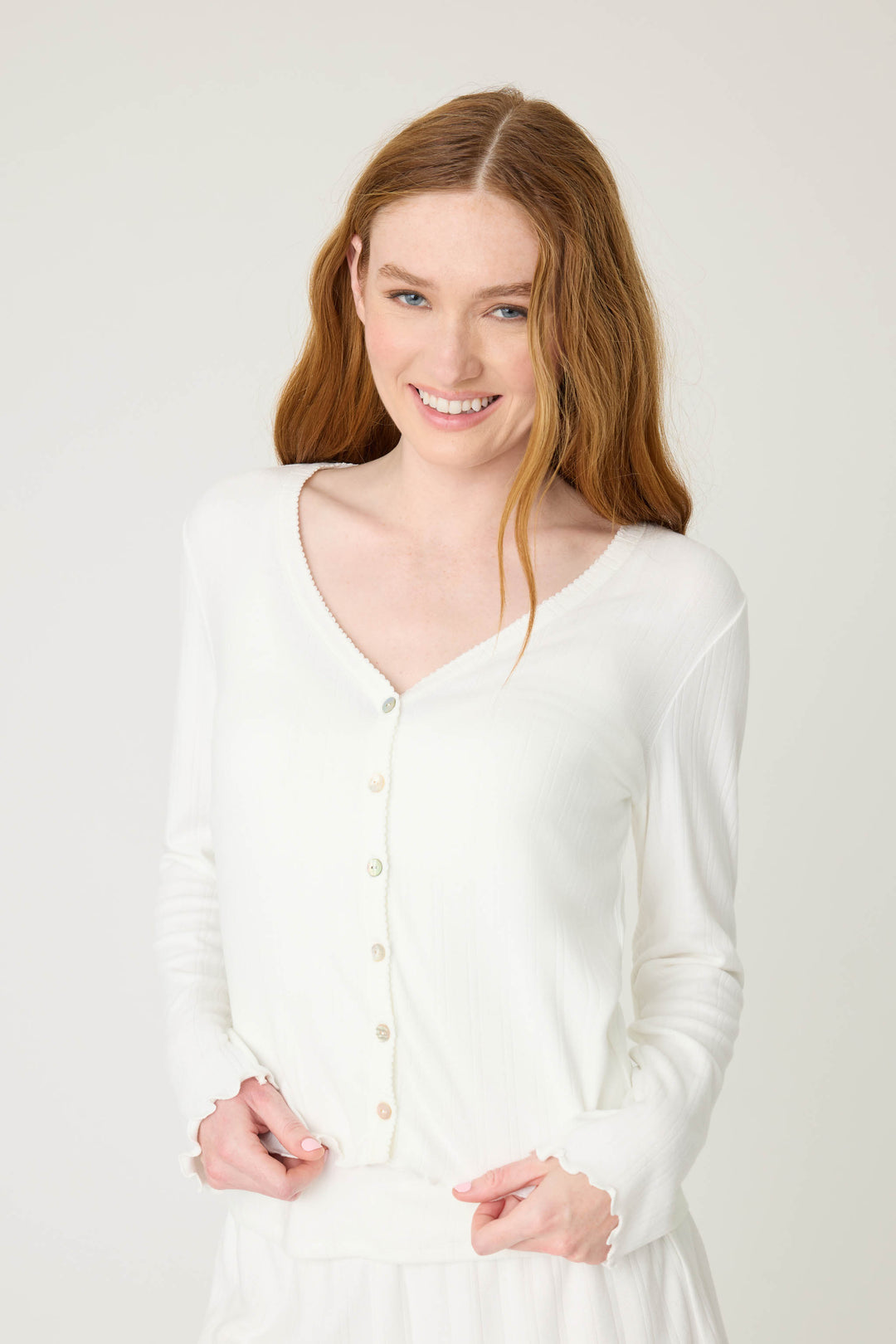 A person with long red hair smiles while wearing the P.J. Salvage Pointelle Essentials Solid Ivory Cardigan against a plain light background.