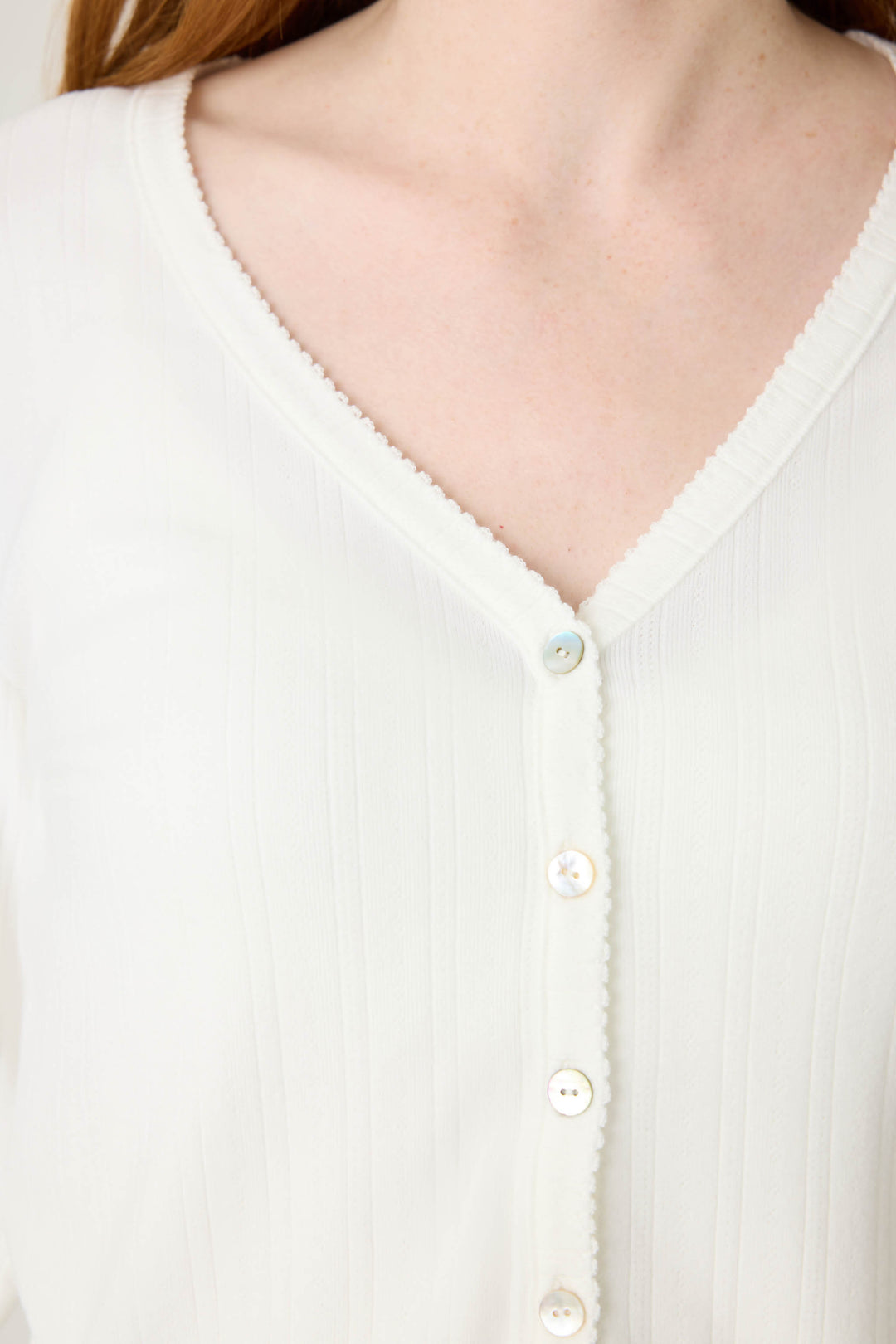 Close-up of a person wearing the Pointelle Essentials Solid Ivory Cardigan by P.J. Salvage, featuring ribbed fabric, a V-neck with delicate trim, and small white buttons down the front for subtle texture and style.