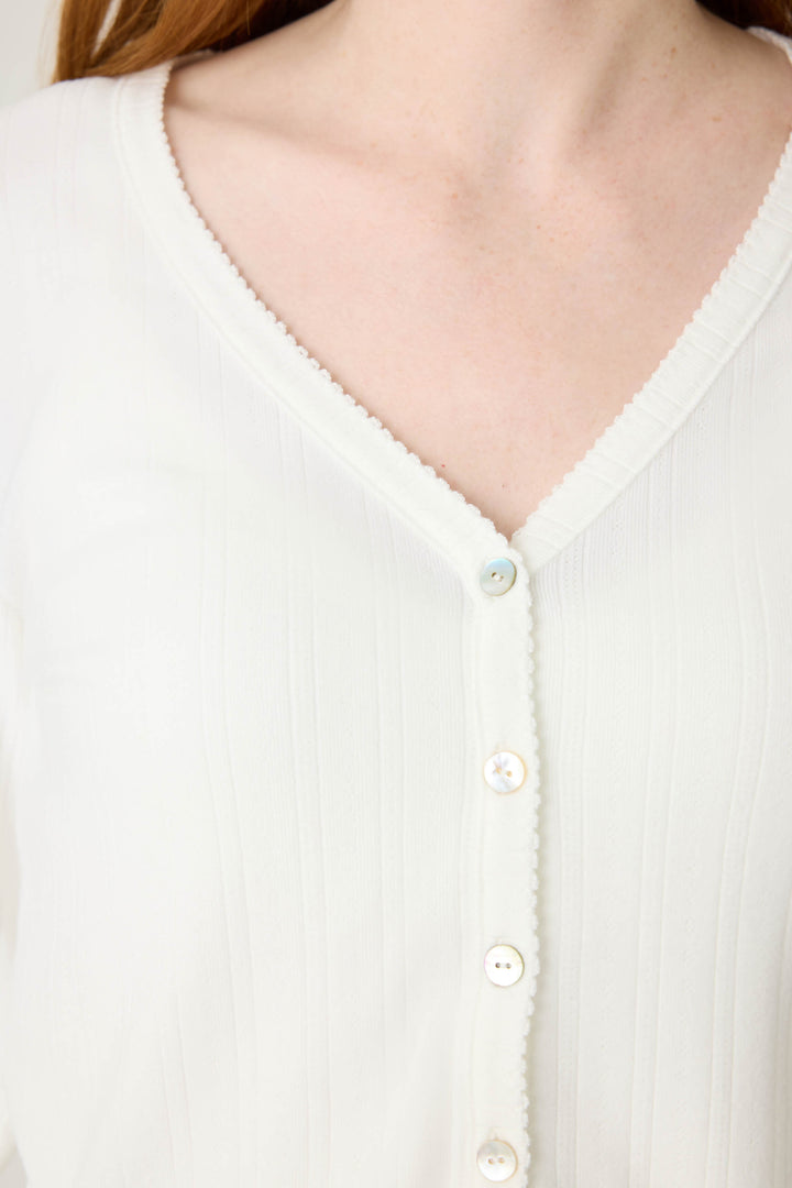 Close-up of a person wearing the Pointelle Essentials Solid Ivory Cardigan by P.J. Salvage, featuring ribbed fabric, a V-neck with delicate trim, and small white buttons down the front for subtle texture and style.