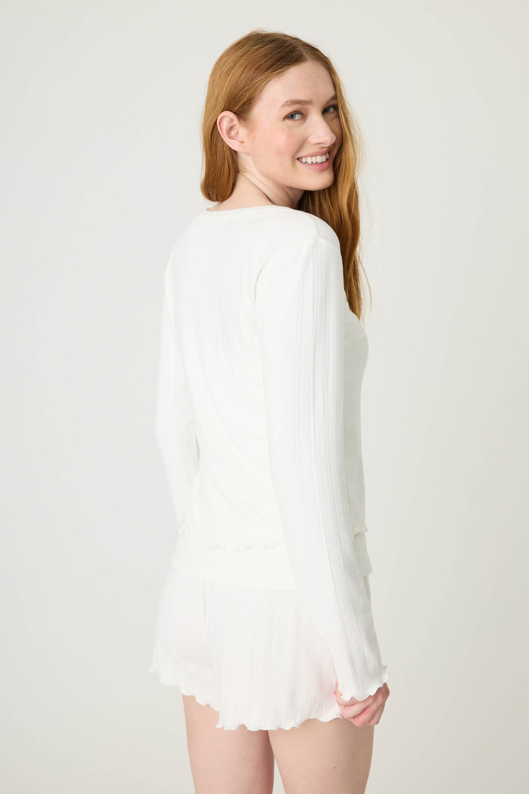 A person with long red hair, wearing the P.J. Salvage Pointelle Essentials Solid Ivory Cardigan, stands facing slightly away and smiles over their shoulder against a plain light background.