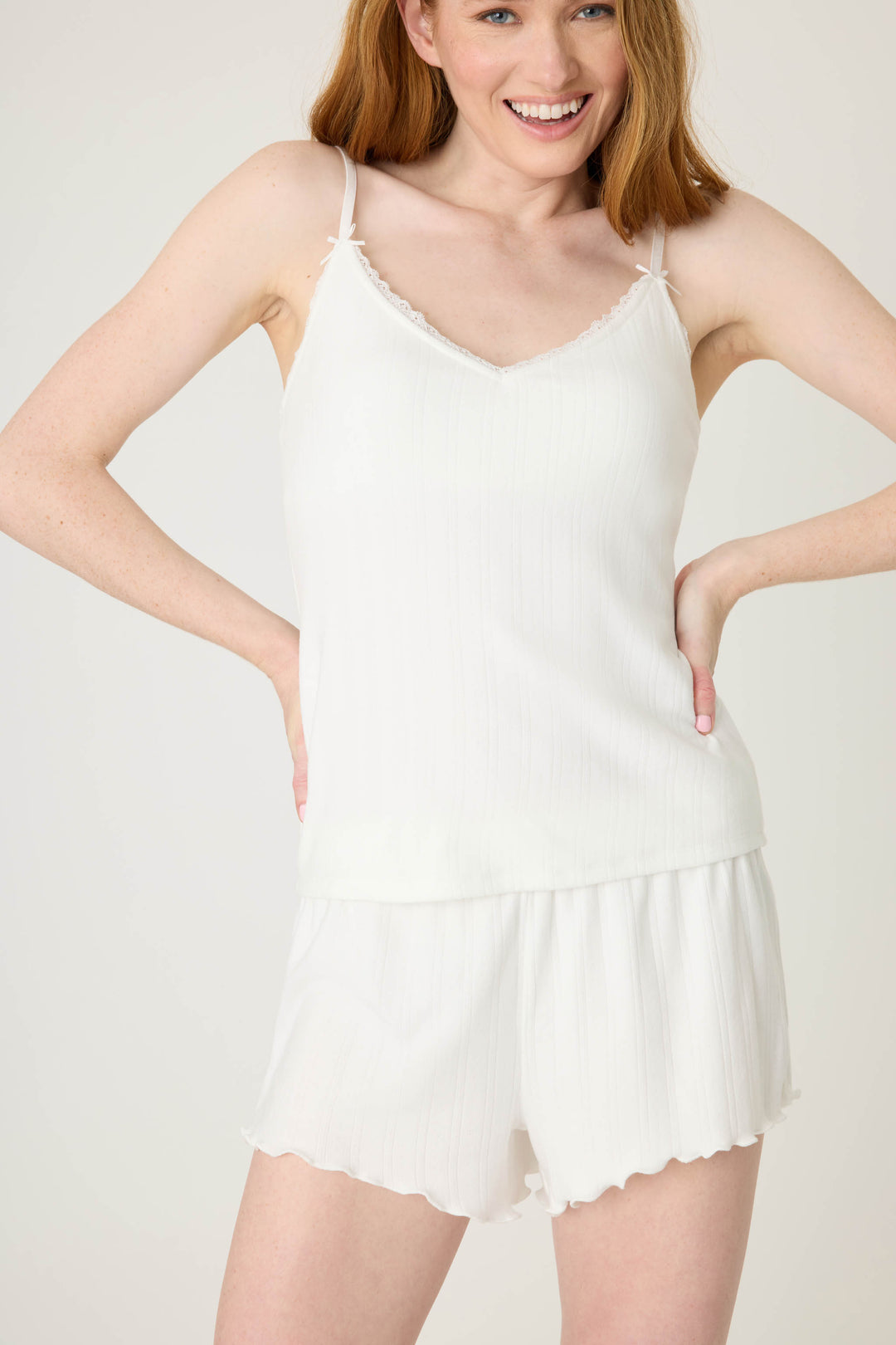 A woman smiles with her hands on her hips, wearing the P.J. Salvage Pointelle Essentials Solid Ivory Camisole and matching shorts, standing in front of a plain light background.