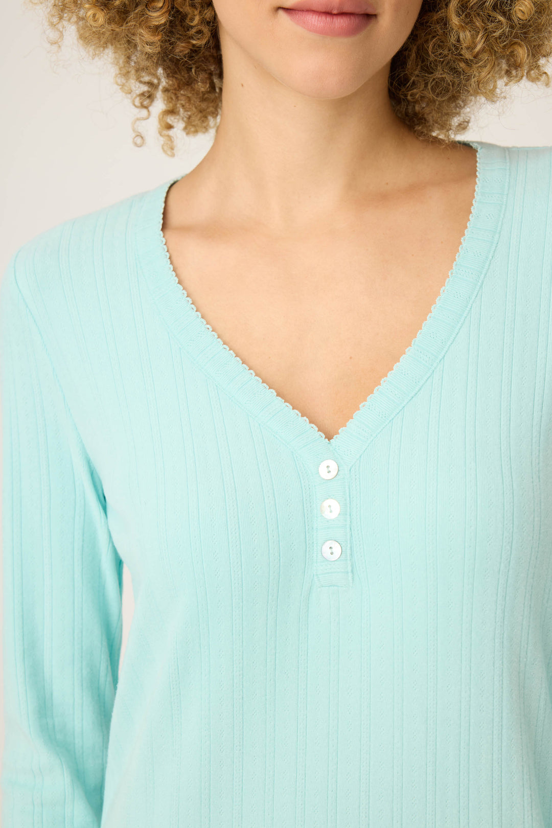 A woman with curly hair wears the P.J. Salvage Pointelle Essentials Solid Mint Night Shirt, a light blue, ribbed, long-sleeve top with a V-neck and four white buttons. Only her upper torso and lower face are visible.
