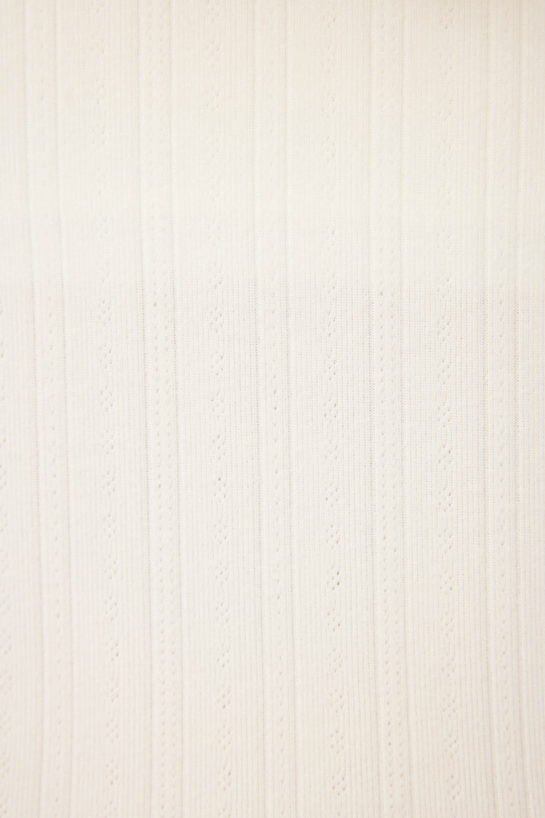 A close-up of P.J. Salvages Pointelle Essentials Solid Ivory Open Leg Pant shows off-white fabric with vertical textured stripes and evenly spaced eyelet patterns.
